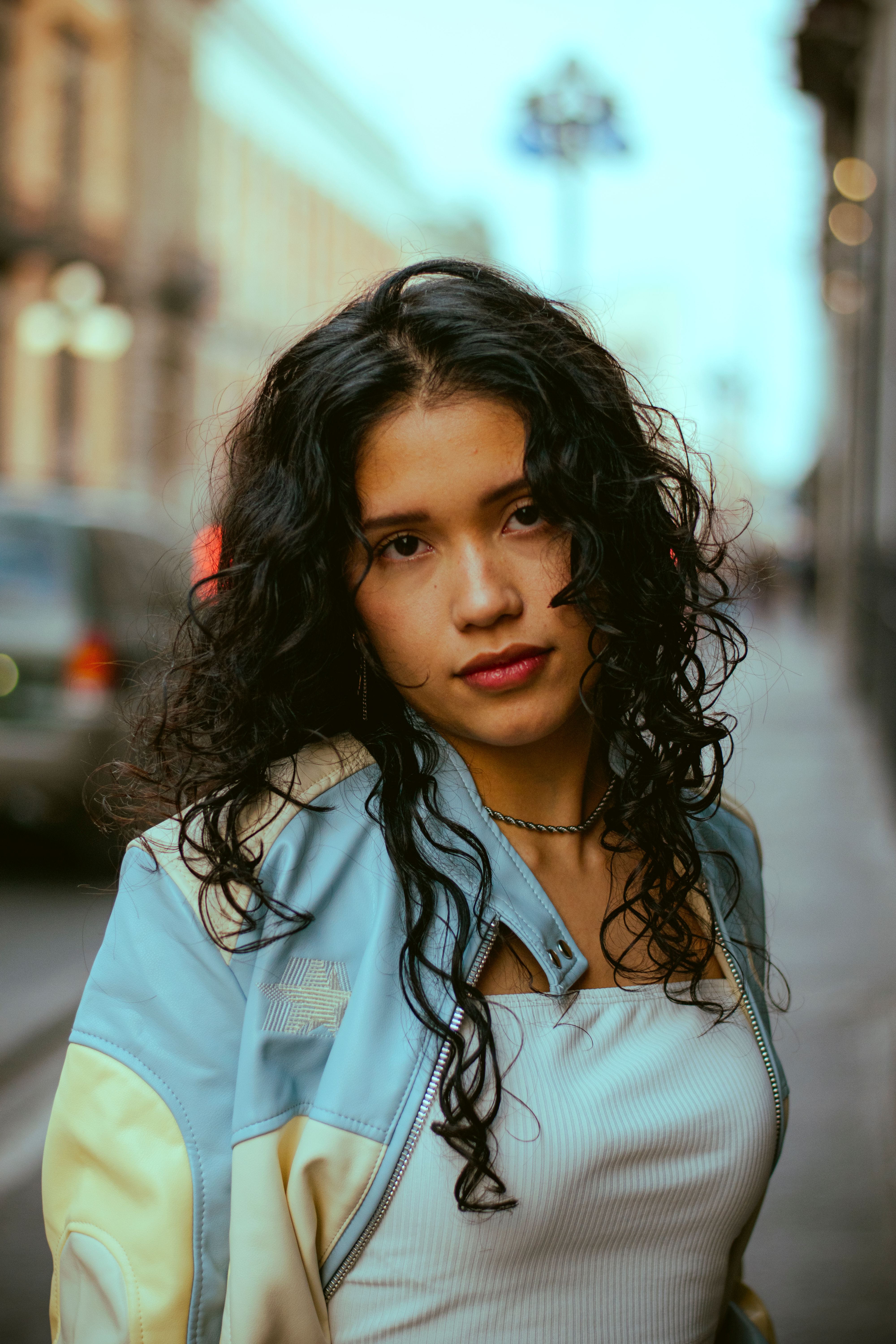 Portrait of a young woman with curly hair in an urban street setting, during the day.
