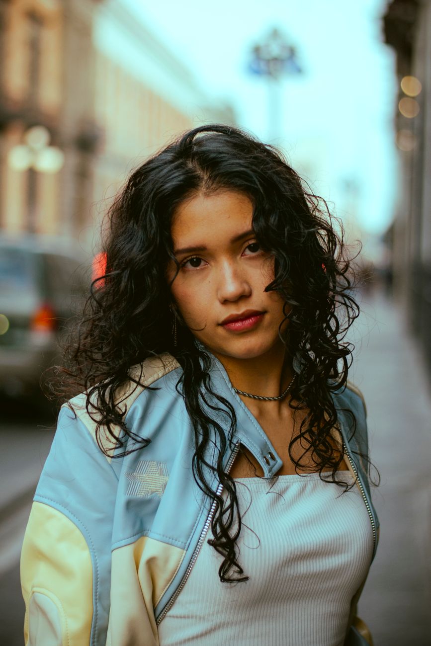 Portrait of a young woman with curly hair in an urban street setting, during the day.