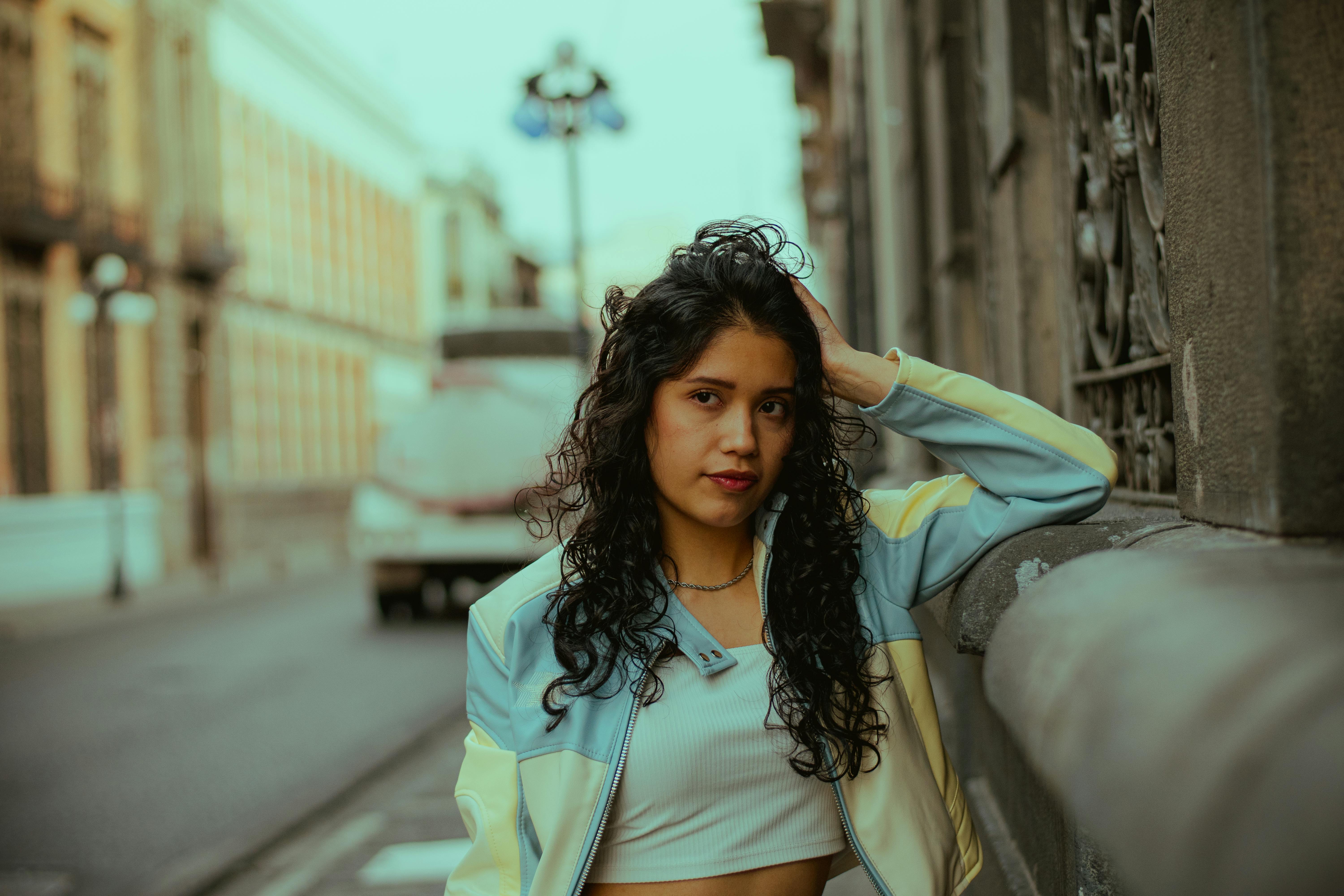 Portrait of a young woman casually leaning against an urban wall in a city setting.