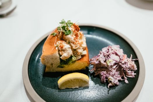 A delectable lobster roll served with coleslaw and lemon wedge, perfect for seafood lovers.