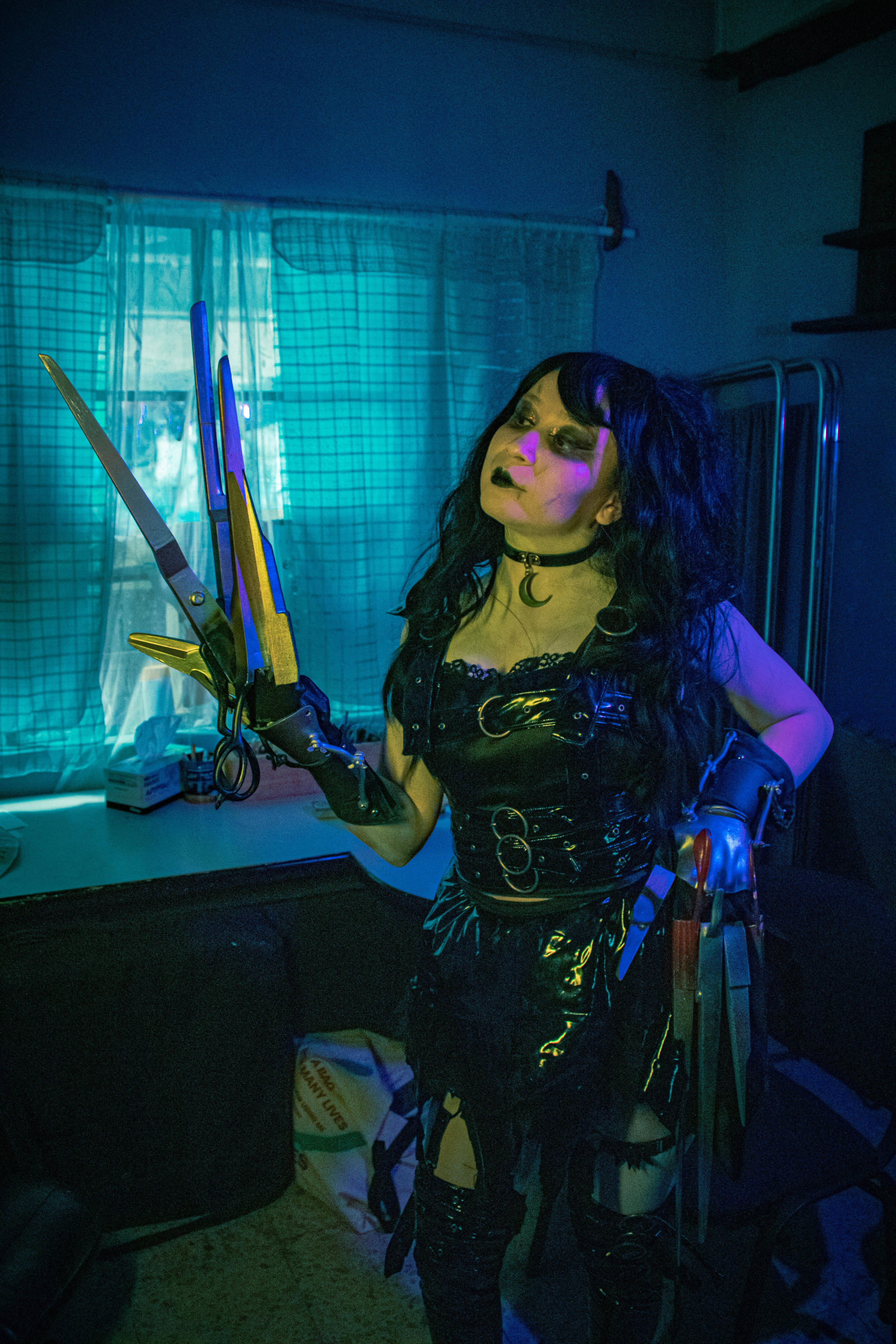 A character in a Gothic cosplay costume with scissor hands in a dark, moody room setting.