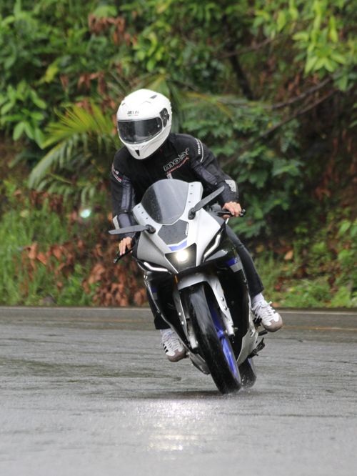 Free A motorcyclist skillfully rides through a wet road curve amid lush greenery, emphasizing speed and caution. Stock Photo