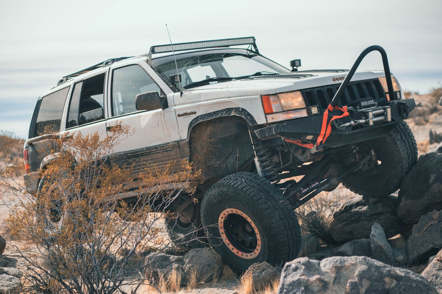 Lifted Jeep Grand Cherokee climbing a boulder field with one front wheel articulating over a rock, showing off-road traction and differential lock in action