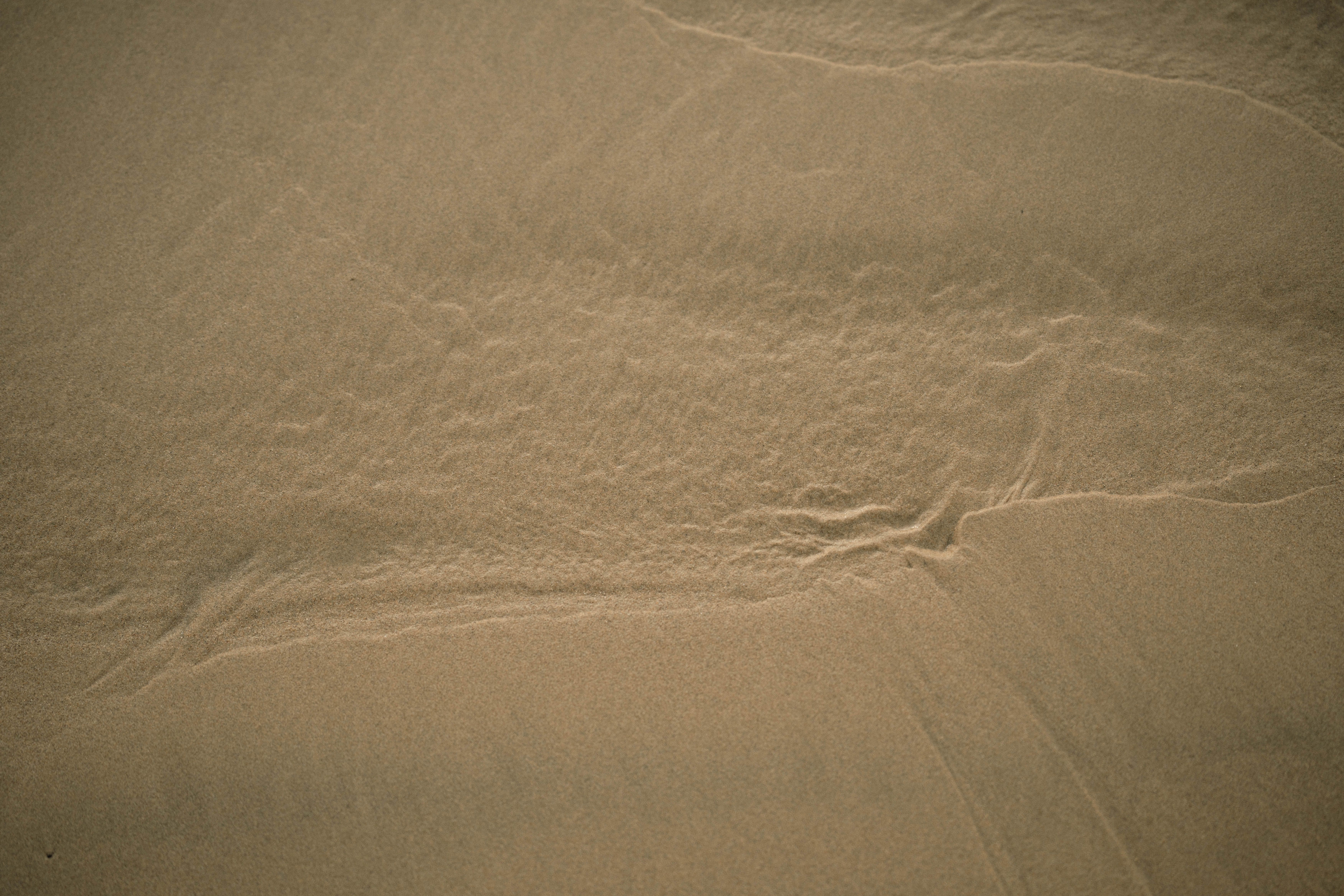 Close-up of sand texture with subtle watermarks, captured at a tranquil beach during sunset.