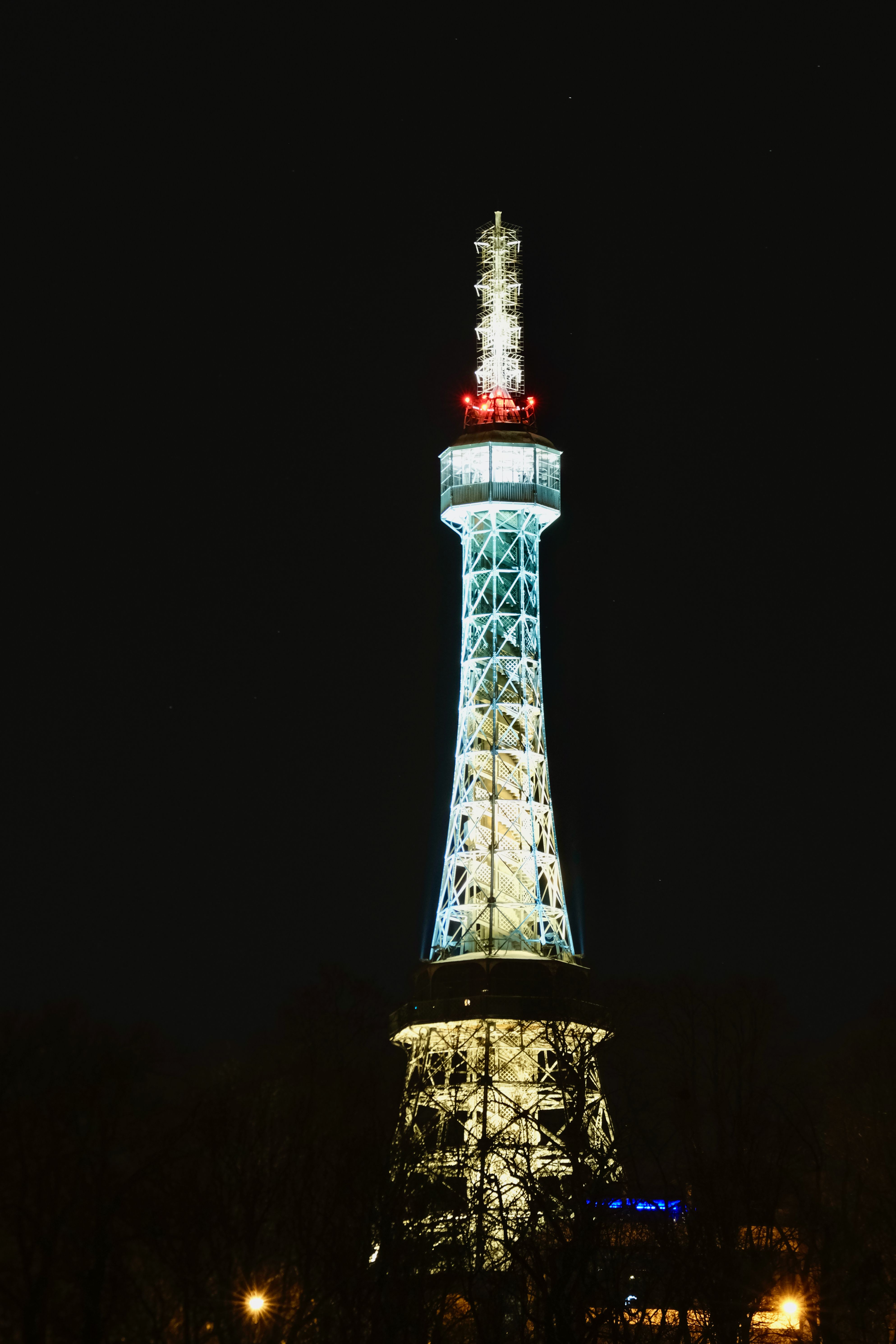 Petřín Tower at golden hour with Prague cityscape views, mirror maze entrance, and Petřín Hill gardens glowing in warm morning light