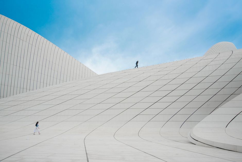 A striking modern architectural structure with people walking across its curves under a clear blue sky.