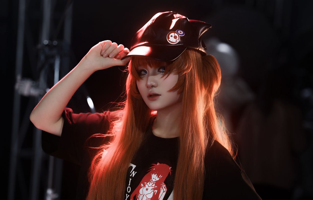 a young adult posing in cosplay attire with a cap and vibrant red hair
