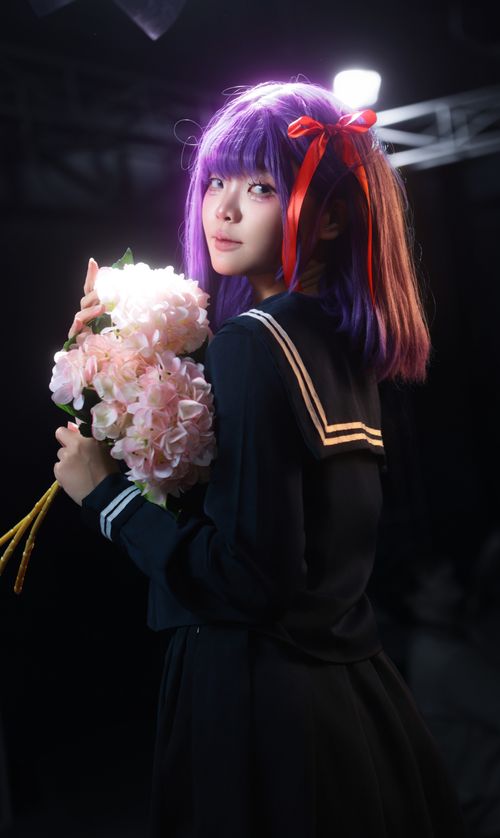 Free Anime-inspired cosplay featuring purple-haired character holding pink flowers in a studio setting. Stock Photo