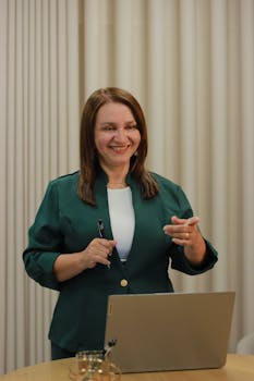 Confident woman in a green blazer giving a presentation in a modern office setting.