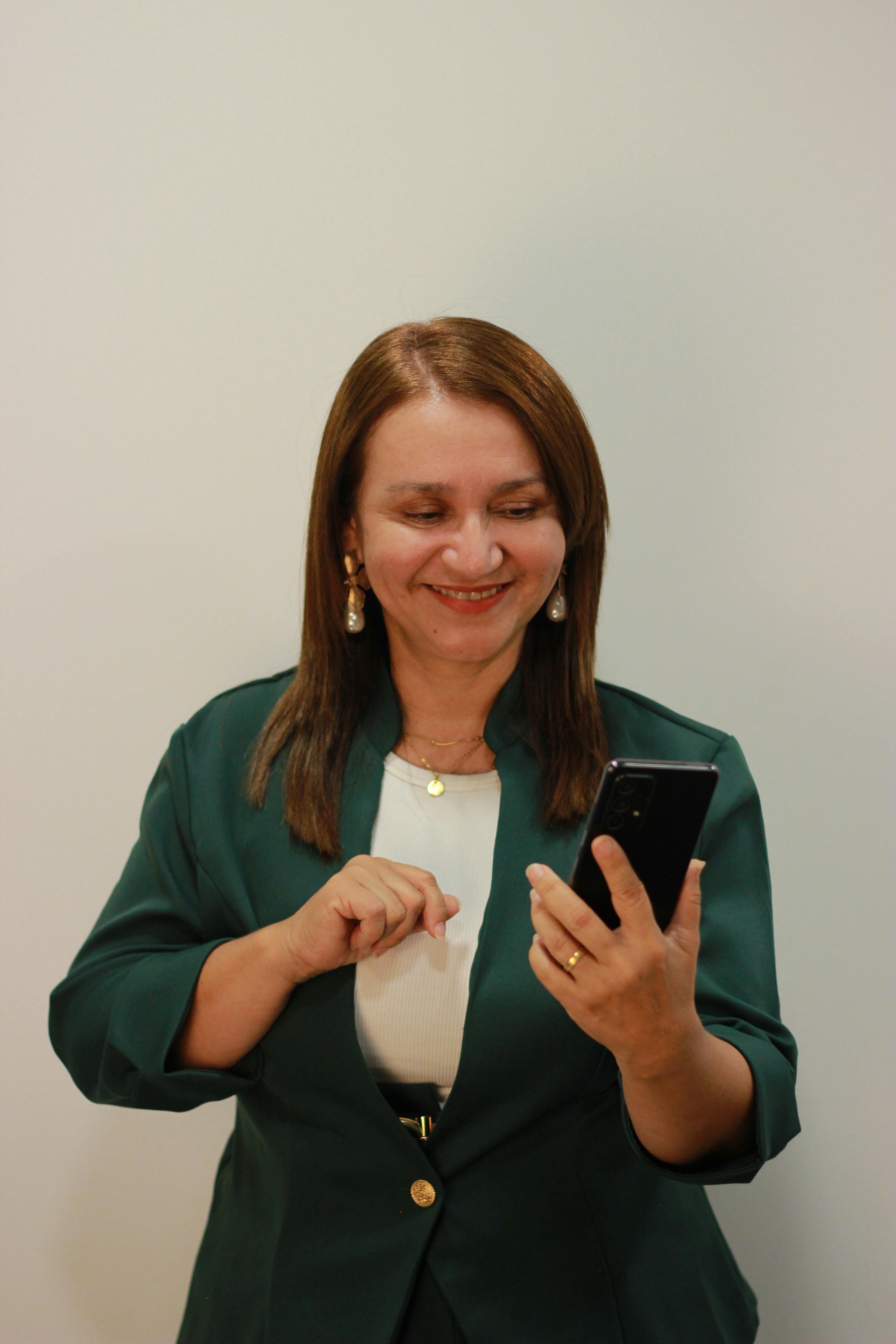 Kostenlos Eine lächelnde Frau in Berufskleidung benutzt ihr Smartphone im Haus. Stock-Foto