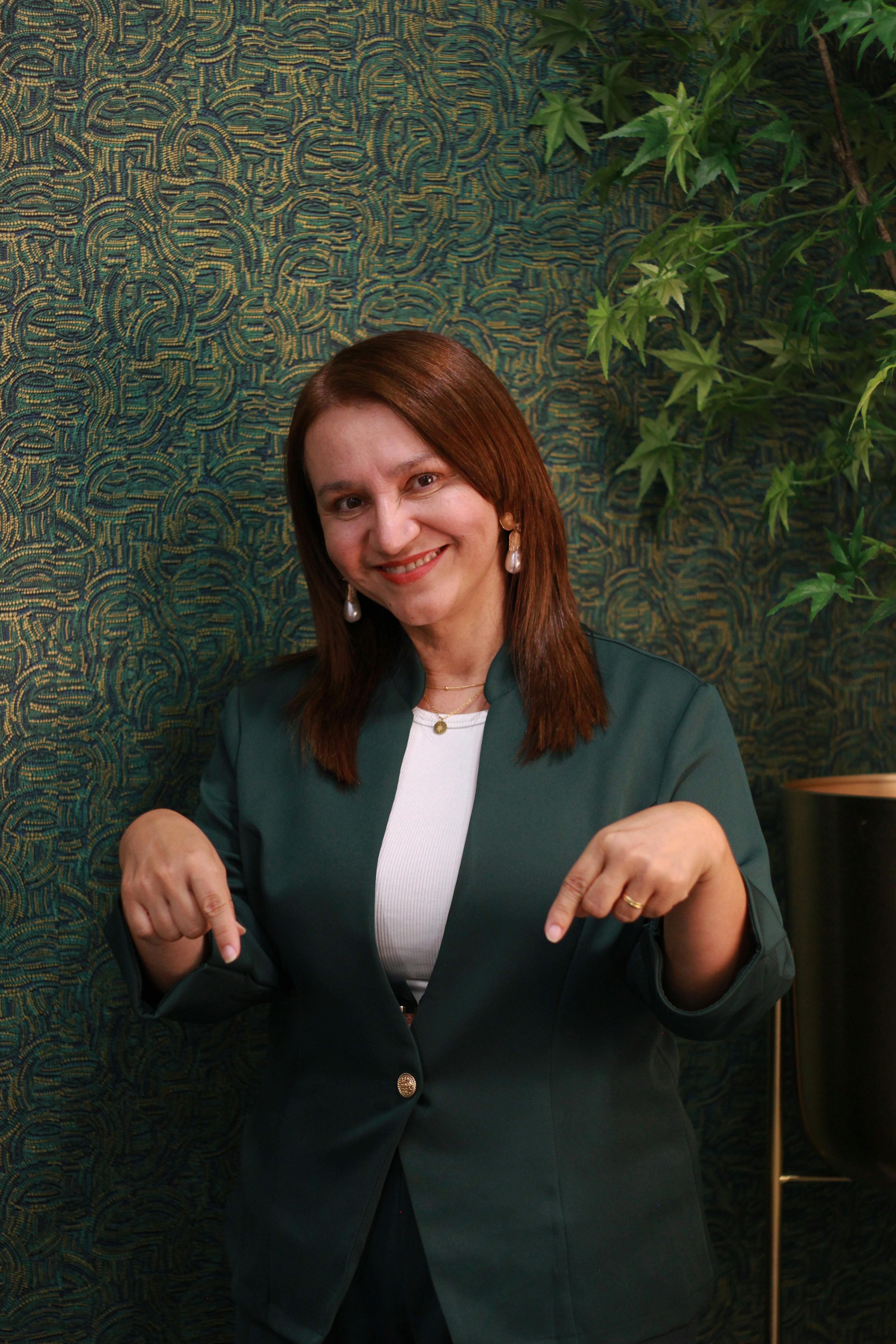 Portrait of a smiling professional woman in a green suit standing indoors against a patterned wall.