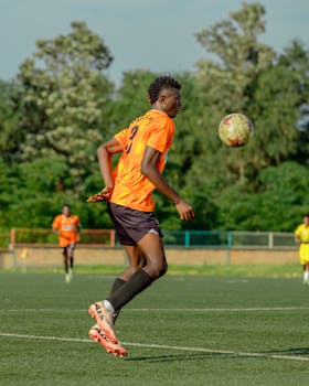 A soccer player in orange kit skillfully controlling the ball on a sunny day.