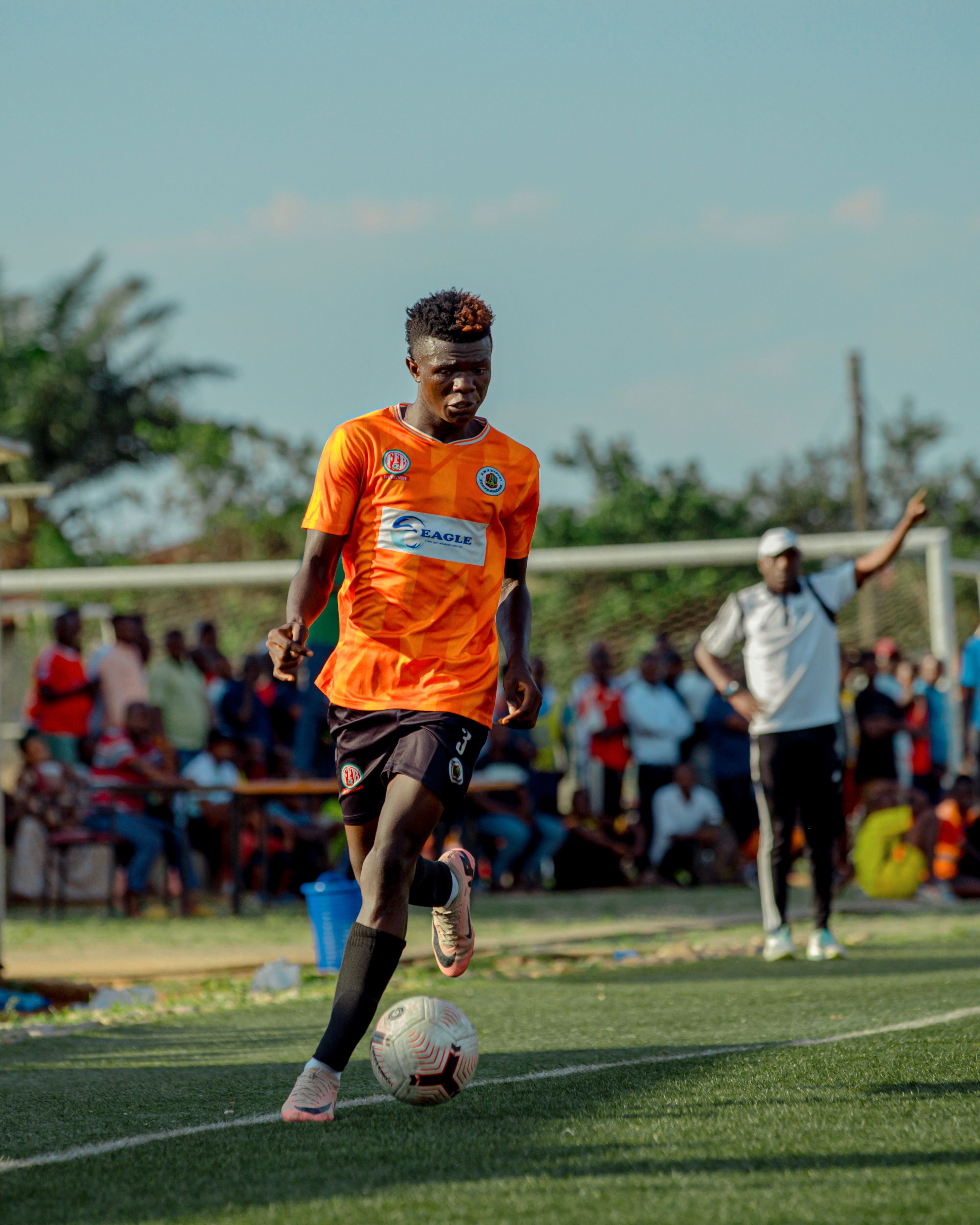 Male soccer player dribbling during an outdoor match with audience in background.