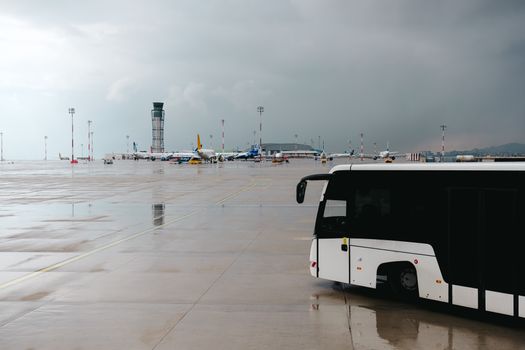 Rainy airport tarmac featuring a passenger bus with airplanes in the background.