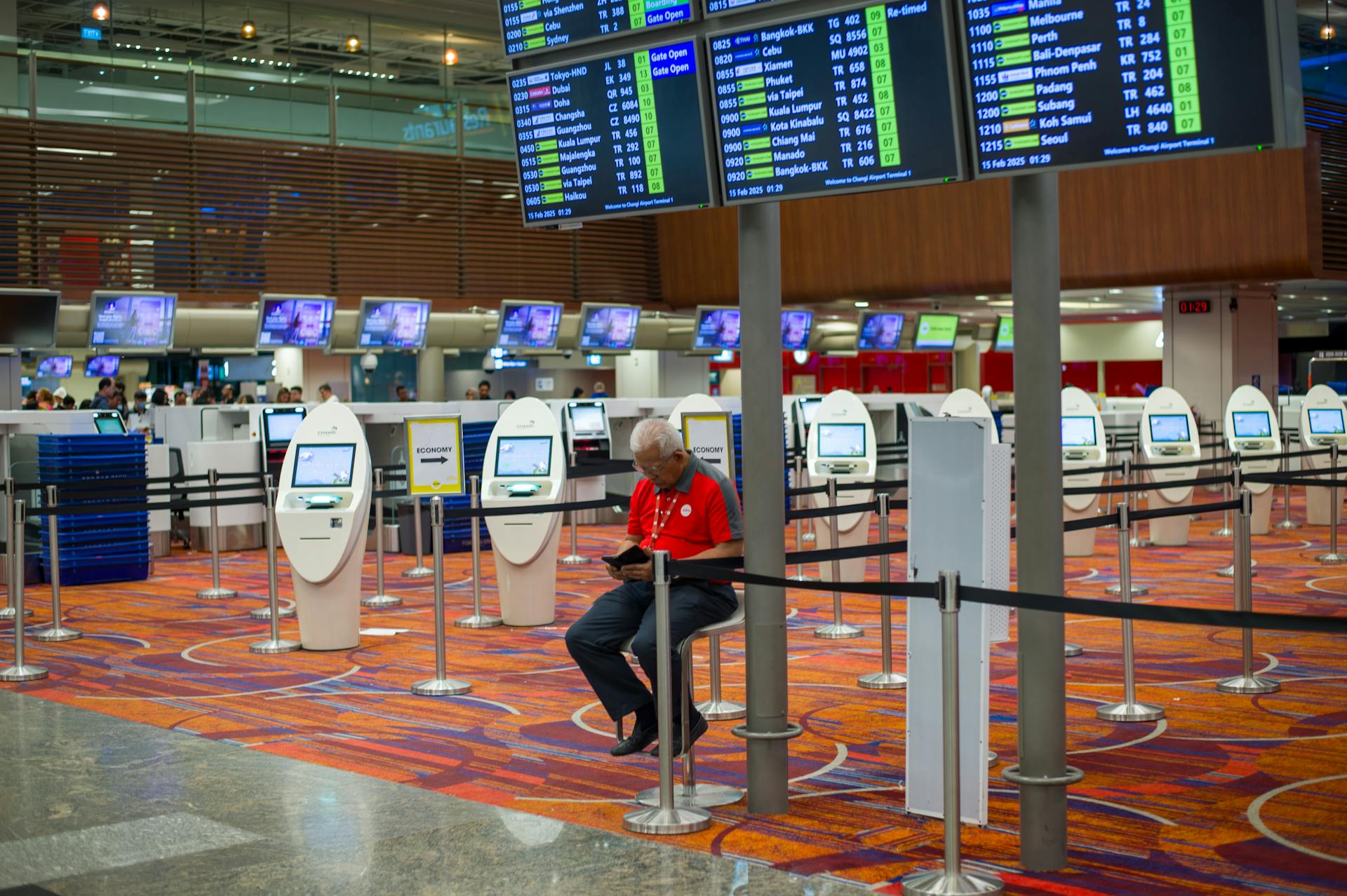 Busy airport terminal interior with flight information displays and check-in kiosks.