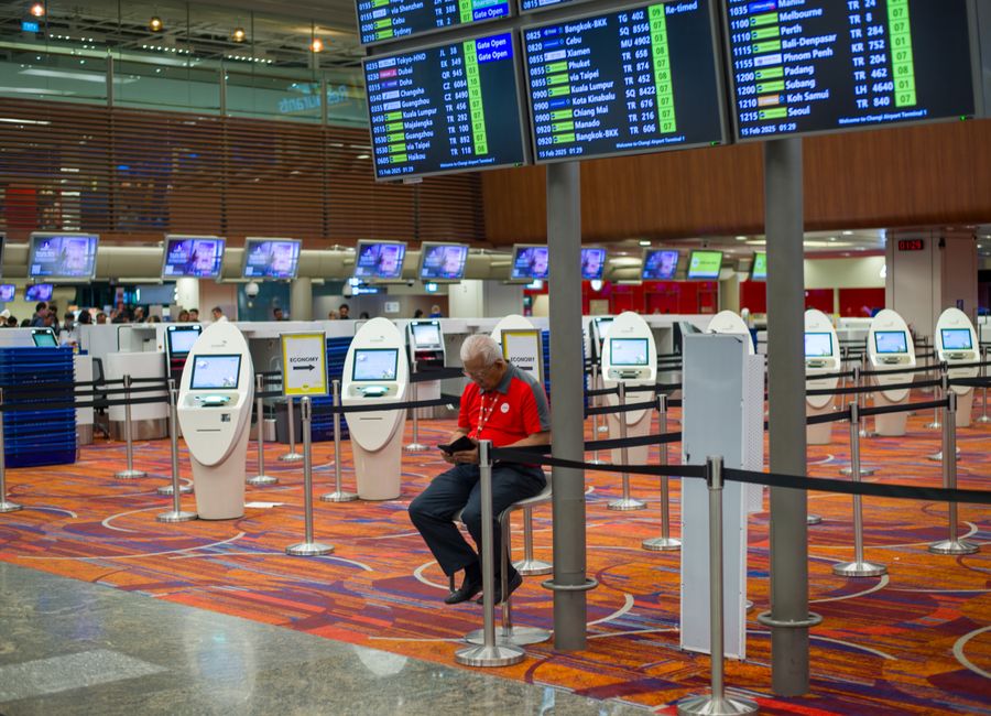 Busy airport terminal interior with flight information displays and check-in kiosks.
