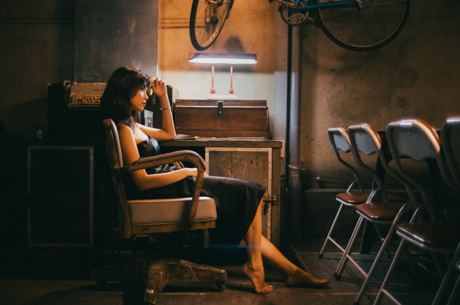 薄暗い、落ち着いた雰囲気のヴィンテージルームで、考えながら座っている女性。