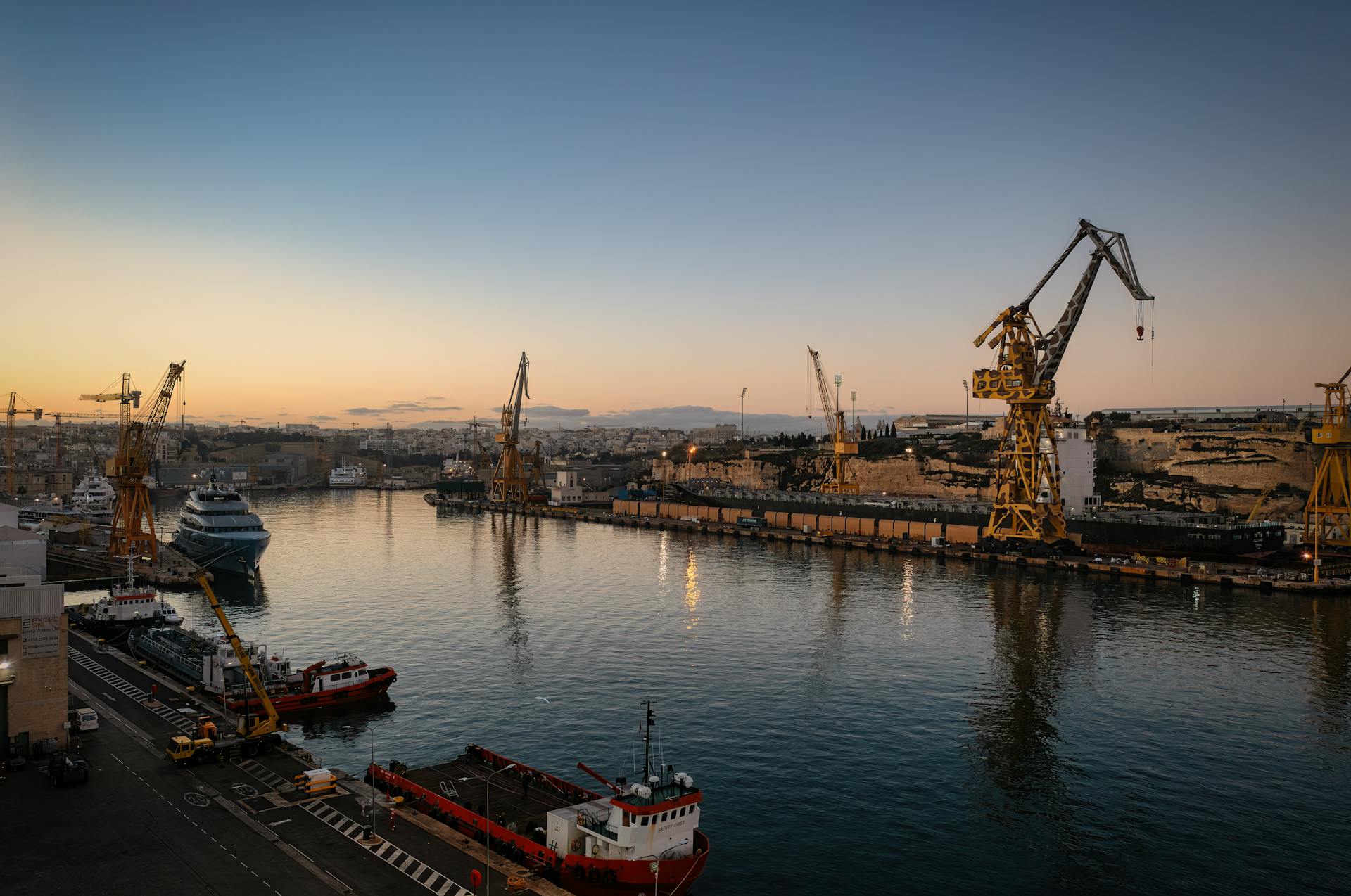 Sunset view of a dockyard with cranes and ships in Malta, reflecting industrial charm.