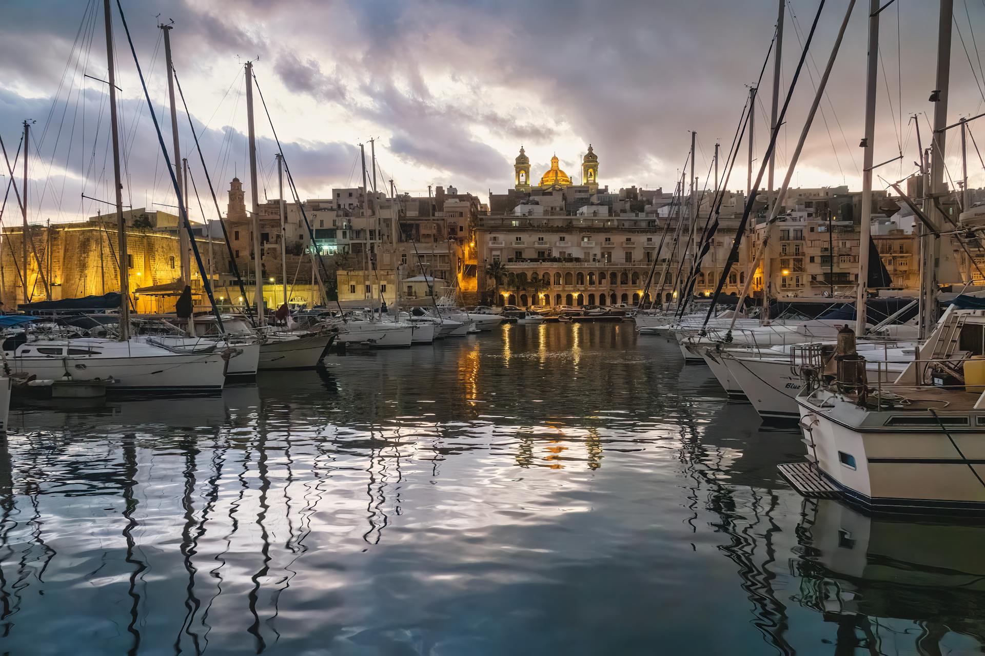 A stunning sunset view of a yacht marina in Malta with historical architecture.