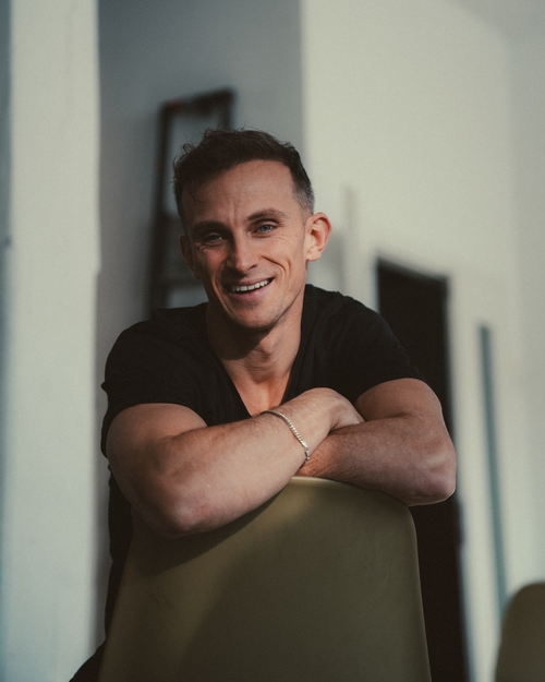 Free Casual portrait of a man smiling, leaning on a chair, in a modern indoor setting. Stock Photo