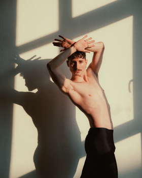 A creative portrait of a male dancer against a sunlit wall creating artistic shadows.