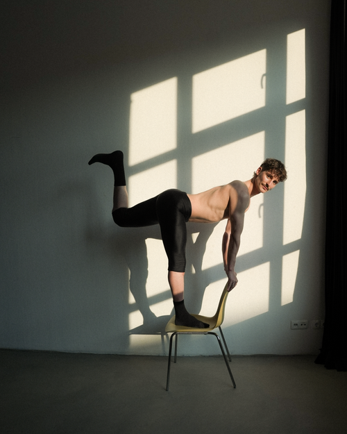 Free A man in athletic wear strikes a dynamic pose on a chair with dramatic window shadows. Stock Photo