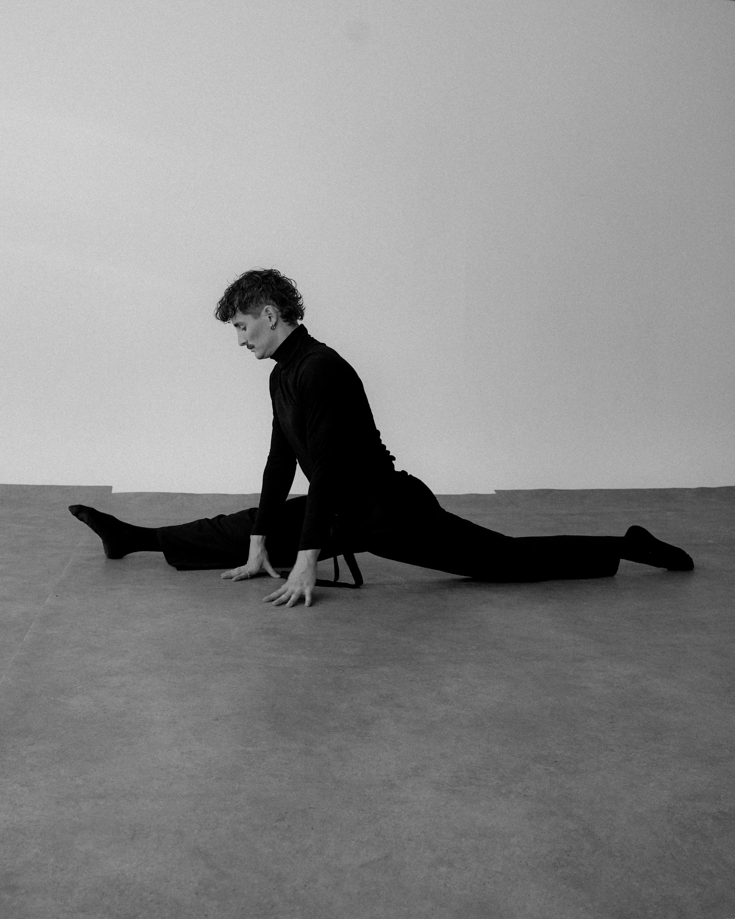 Black and white photo of a male dancer doing the splits on a studio floor.
