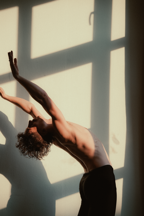 Free A person gracefully stretching into a dance pose with dramatic shadows on the wall. Stock Photo
