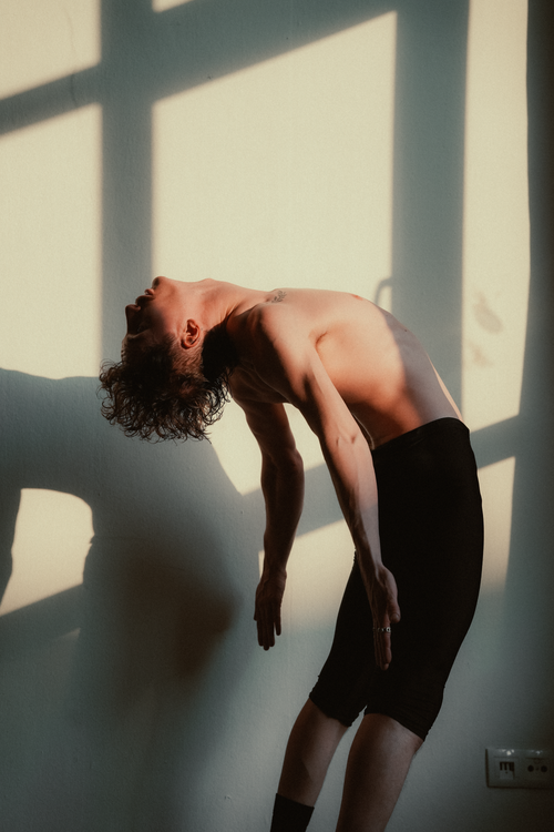 Free A young dancer gracefully bends backward in a bright room with soft natural lighting. Stock Photo