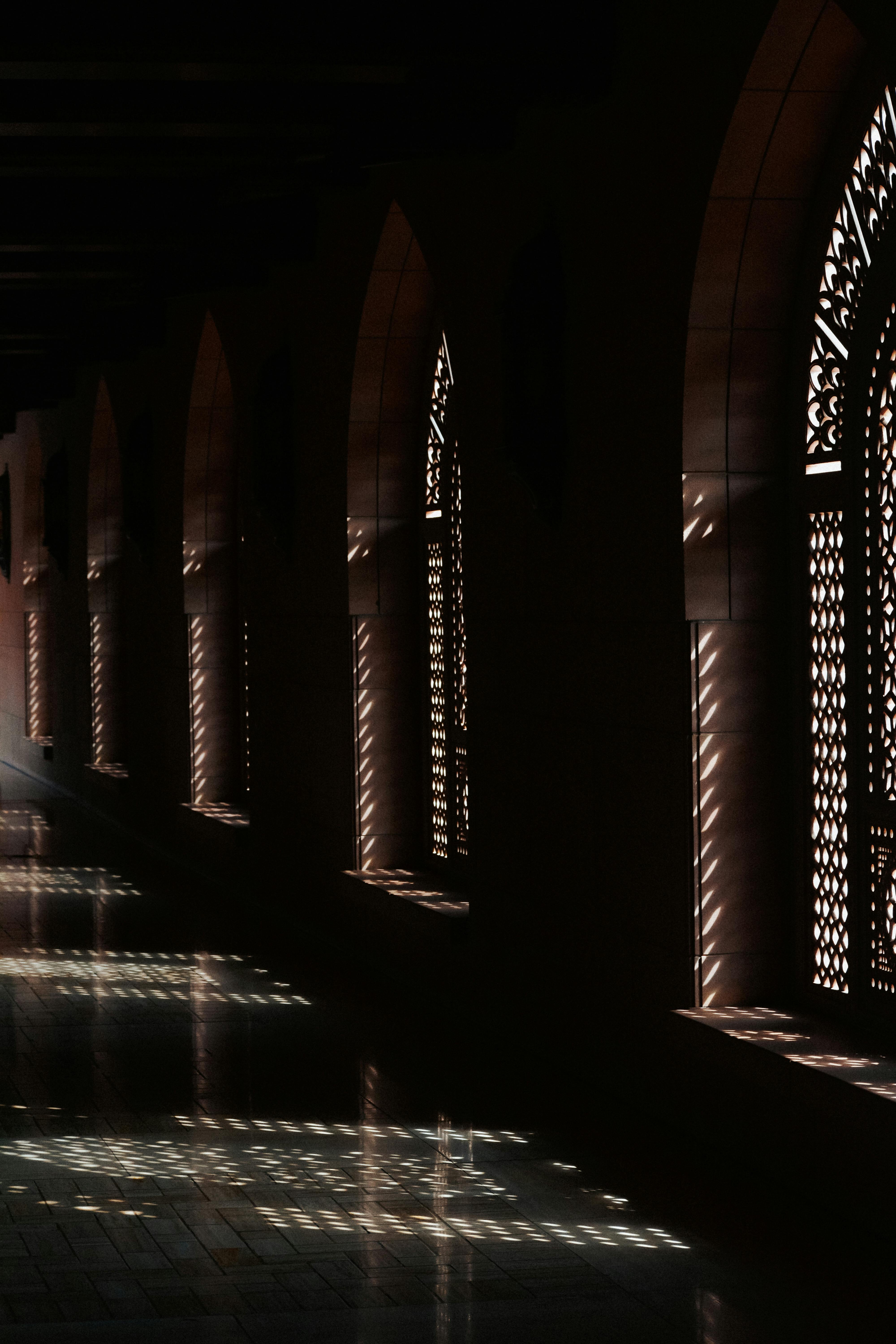 Sunlight casts patterns through ornate arches in an Omani architectural corridor.