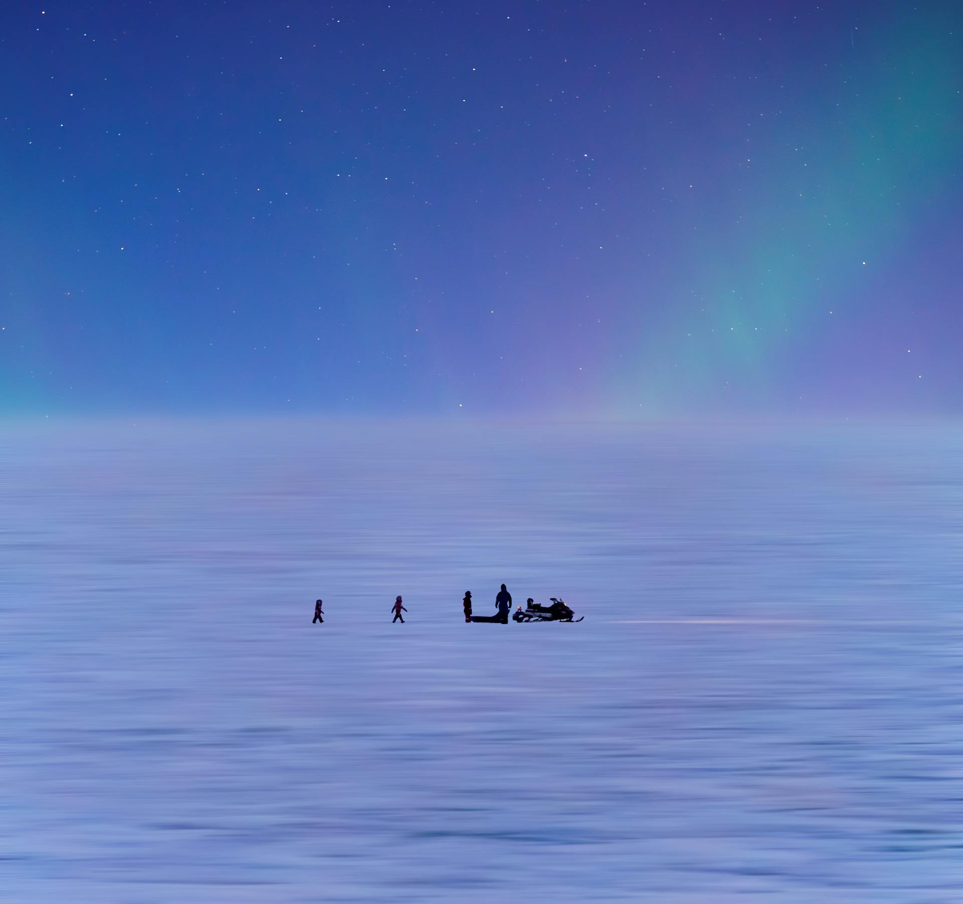 Scenic view of people and snowmobile under northern lights on icy landscape.