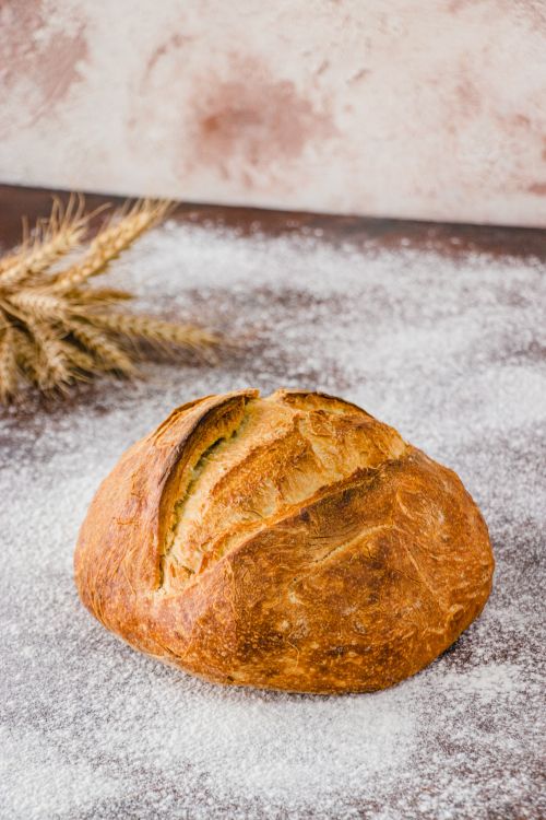 Free Golden brown artisan bread on floured surface with wheat, perfect for baking themes. Stock Photo