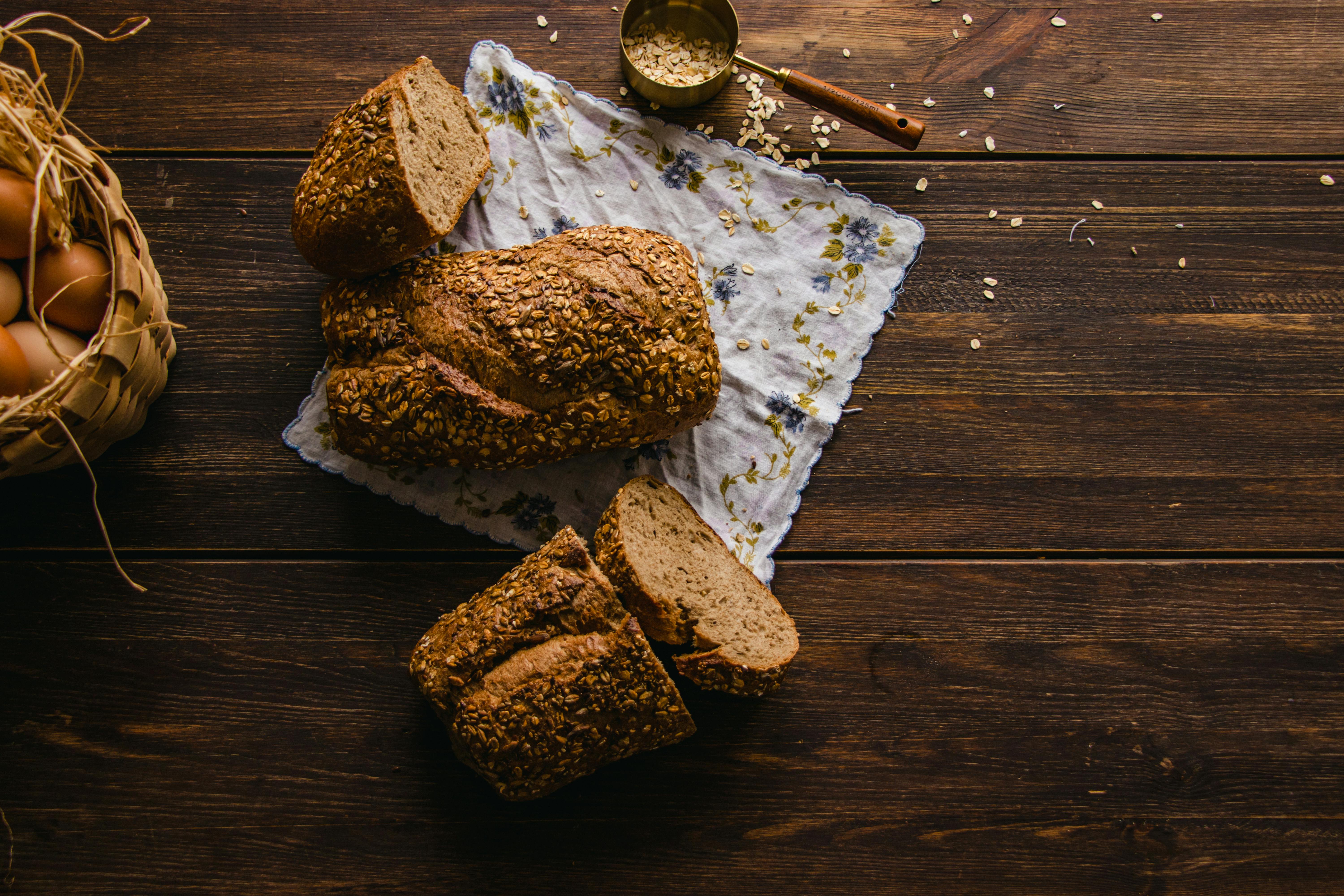 Sliced whole grain bread on a wooden table with a basket of eggs and oats.