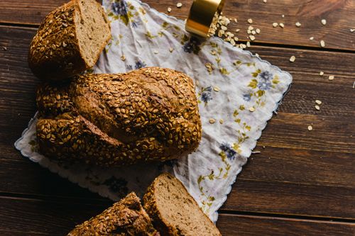 Free A rustic loaf of whole grain bread on a floral cloth, surrounded by oats on a wooden surface. Stock Photo