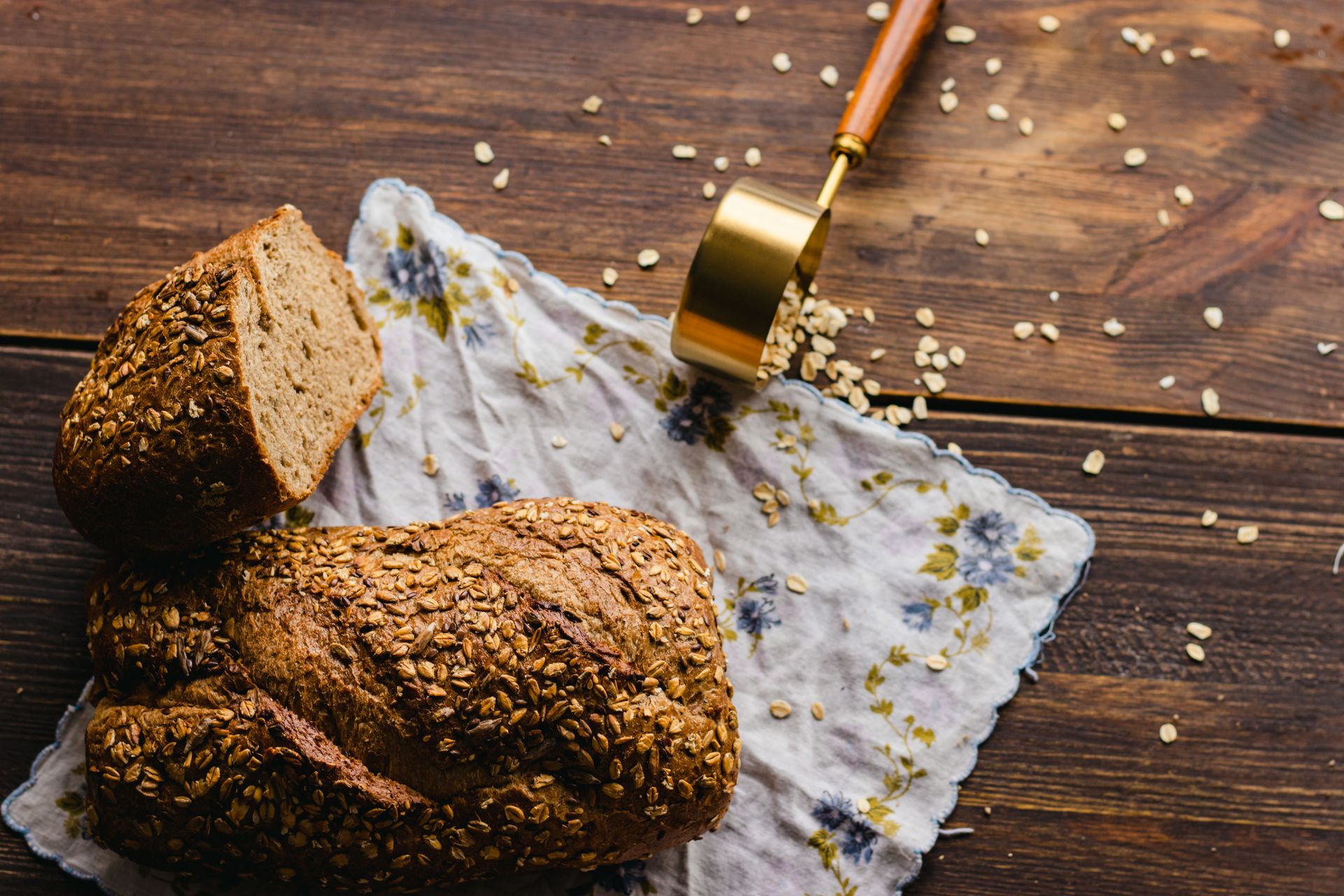 Rustic style whole grain bread loaf with oats on floral cloth and wooden table.