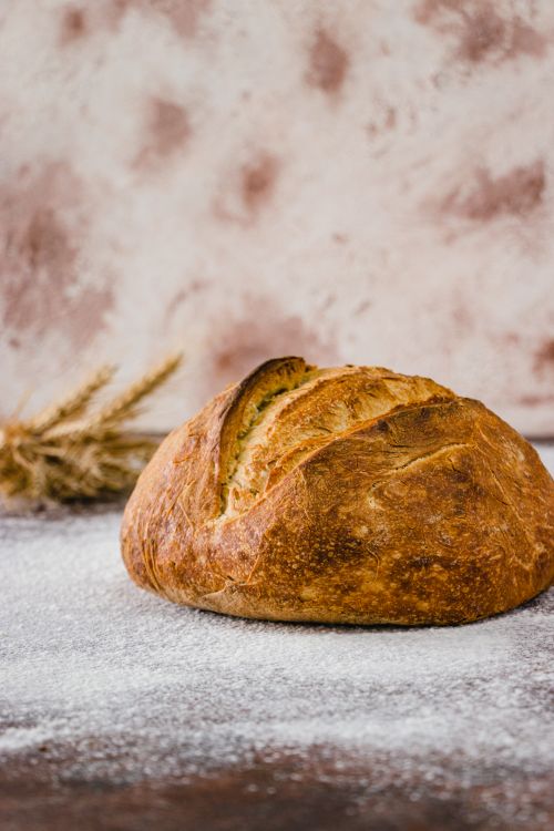 Free Golden brown rustic artisan bread resting on a floured surface, evoking warmth and tradition. Stock Photo