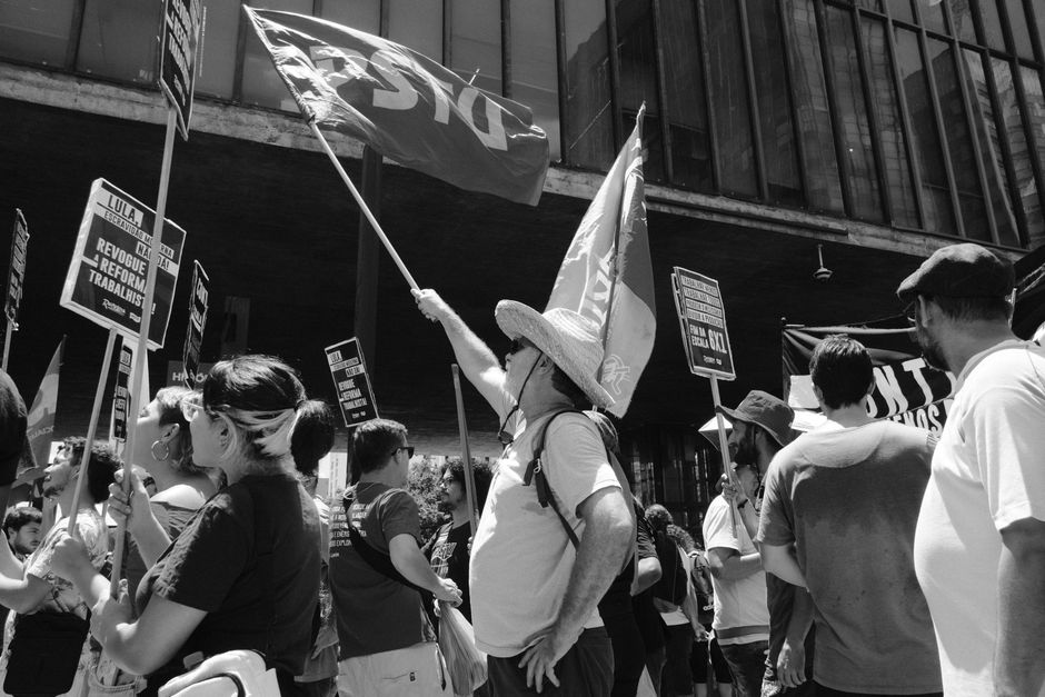 Multitud sostiene banderas y carteles durante protesta en entorno urbano.