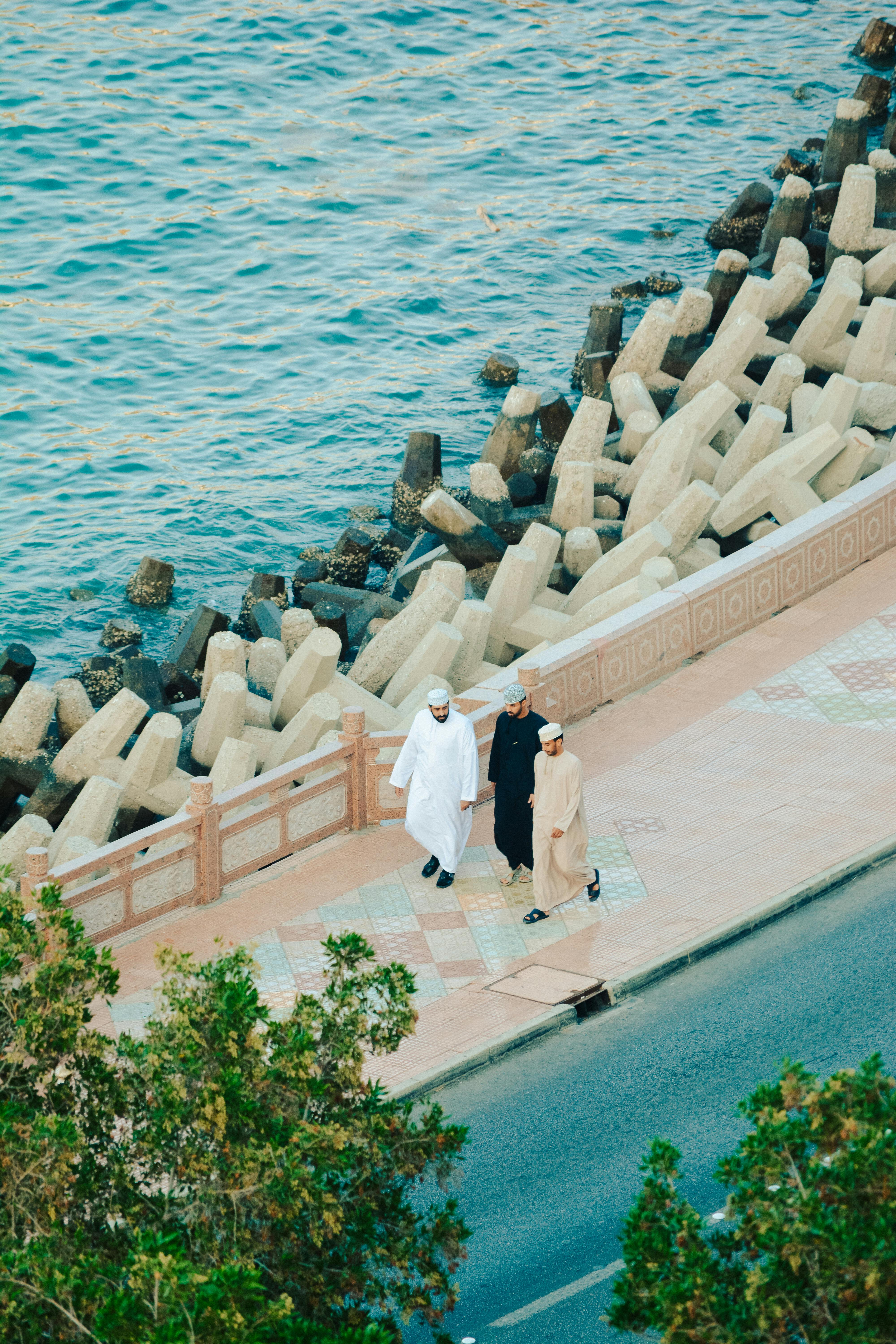 Aerial shot of three people walking along the Omani coast by the sea with distinctive geometric barriers.