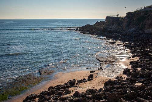 Free Scenic view of Lisbon's rocky beach at sunset, with gentle waves and clear sky. Stock Photo