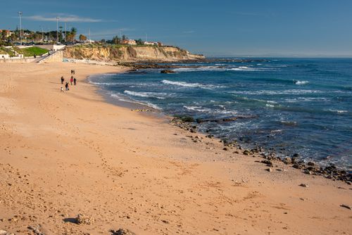 Free A serene sandy beach with cliffs and blue skies in Lisbon, Portugal, captured in daylight. Stock Photo