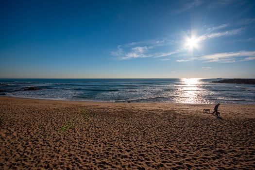 Peaceful beach scene with clear sky and sparkling sea in Lisbon, Portugal.