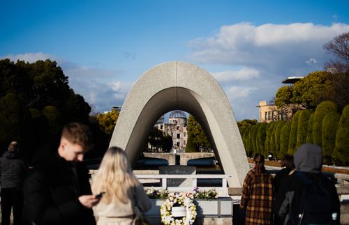 Free Visitors at Hiroshima Peace Memorial Park with cenotaph arch framing the Atomic Bomb Dome in the background. Stock Photo