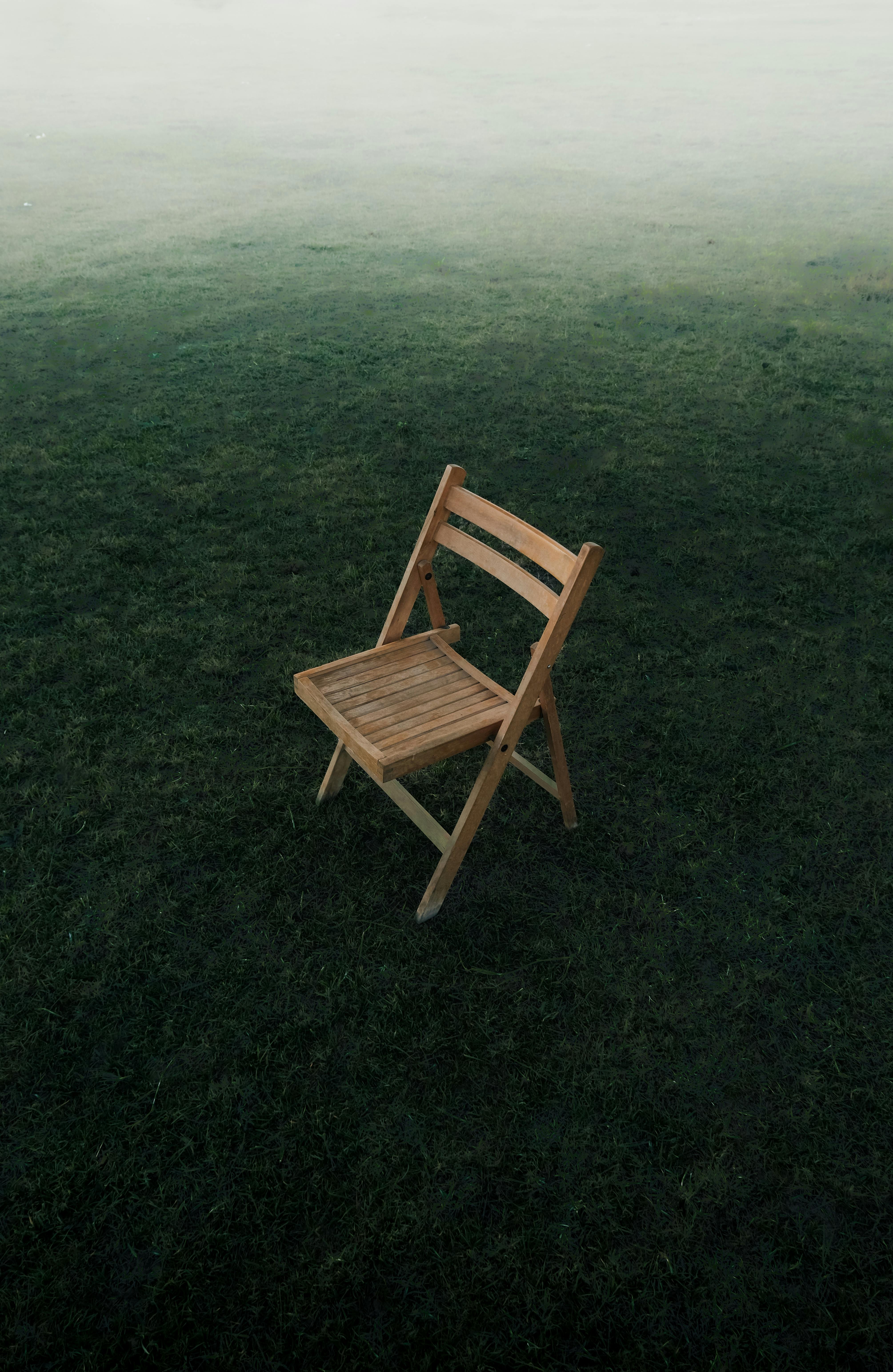 A lone wooden chair sits on a misty grass field, evoking solitude and tranquility.