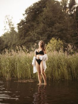 A woman in swimwear stands in calm water, surrounded by lush green reeds.