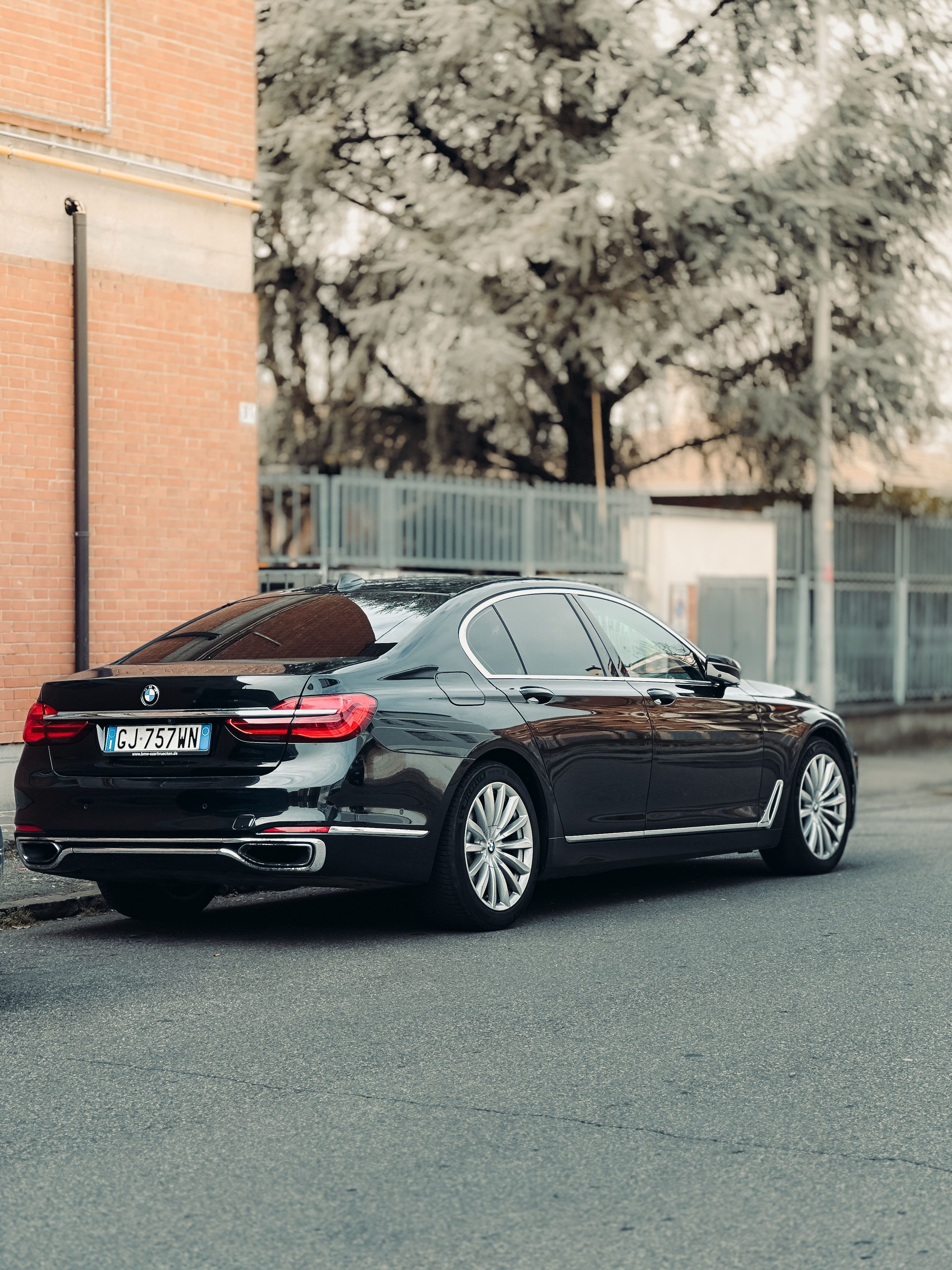Elegant black luxury car parked on a city street surrounded by brick and trees.