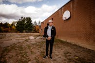 一名穿着休闲装的年轻人站在砖墙边，手里拿着篮球筐