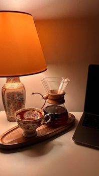Warm lighting illuminating a coffee setup with a vintage cup next to a laptop.