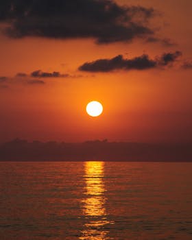 A tranquil sunset over the ocean, reflecting vibrant orange hues on the calm water.