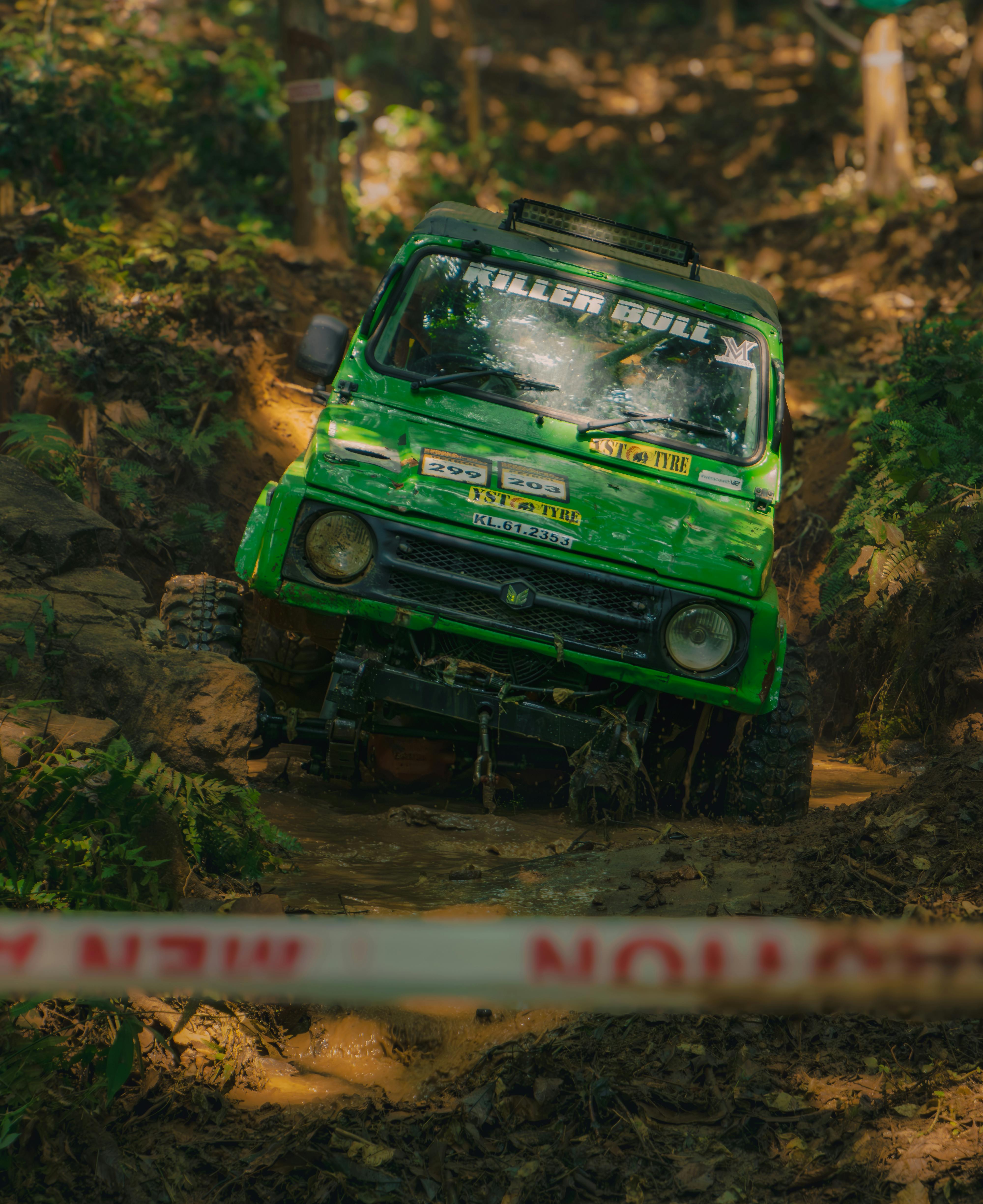 Green 4x4 vehicle tackling muddy and rugged off-road terrain in a dense forest.