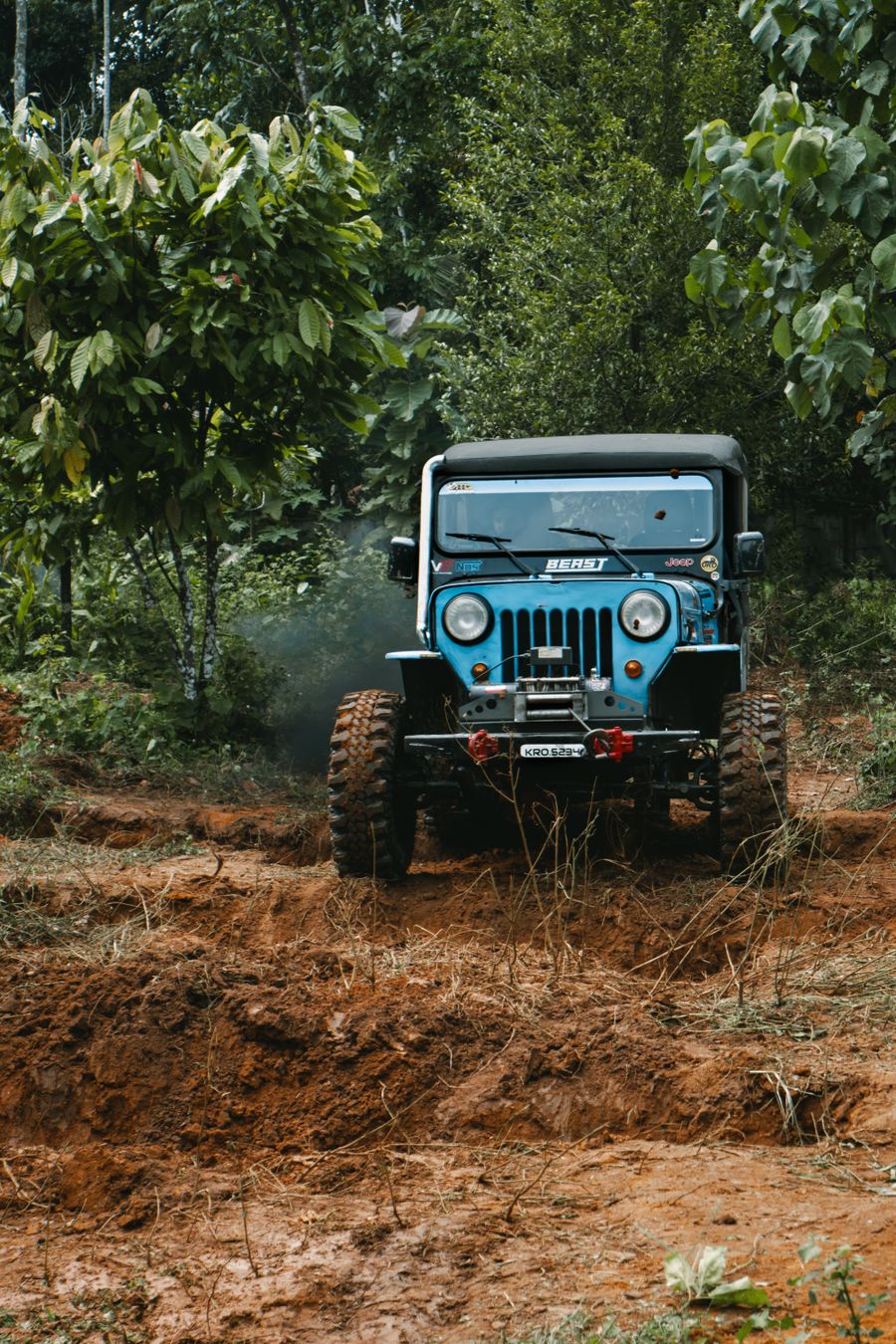Blue off-road jeep driving through forest on a rugged trail